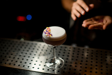 Glass of a delicious violet color cocktail decorated with different flower petals