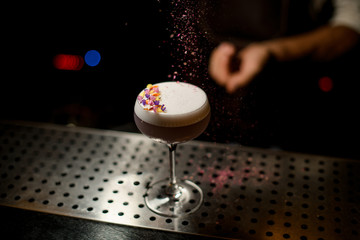 Bartender sprinkling on the cocktail decorated with flower petals a shredded flowers