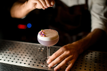 Male bartender sprinkling on the cocktail with white scum decorated with flower petals a shredded flowers