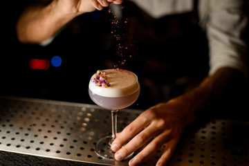 Professional bartender sprinkling on the cocktail with white scum decorated with flower petals a shredded flowers