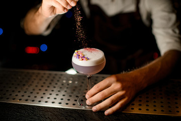 Professional bartender sprinkling on the cocktail decorated with petals a shredded flowers