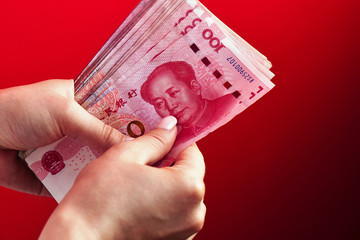 A pile of RMB banknotes of Chinese yuan money in a female hand on a red background - obrazy, fototapety, plakaty