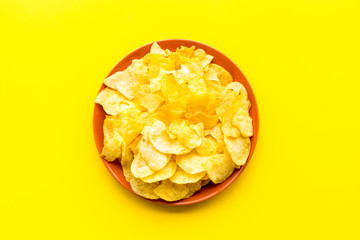 Potato chips in bowl ready to eat on yellow background top view