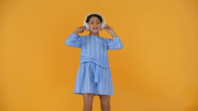 happy preteen child in blue dress listening music in headphones