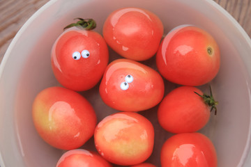 Red tomatoes in water bowl, one with funny doll 's eyes, fresh fruits top view background.