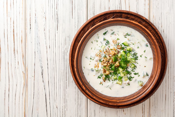 Traditional bulgarian cold summer soup tarator with yogurt, dill, cucumber and walnuts in ceramic bowl on wooden table. Top view. Copy space.