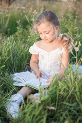 Little girl with a book in her hands on a meadow in a summer day.