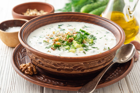 Traditional bulgarian cold summer soup tarator with yogurt, dill, cucumber and walnuts in ceramic bowl on wooden table. Selective focus.