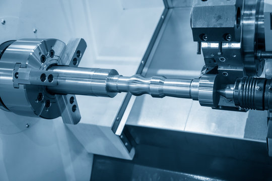 The operation of CNC lathe machine cutting the metal shaft parts in the light blue scene. The hi-technology mechanical parts manufacturing process by CNC turning machine.