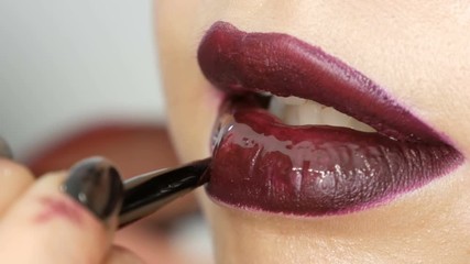 Juicy dark black red lips are made up with special brush lipstick and lip gloss, which is applied by a professional makeup artist. High fashion, girl model lips close up view