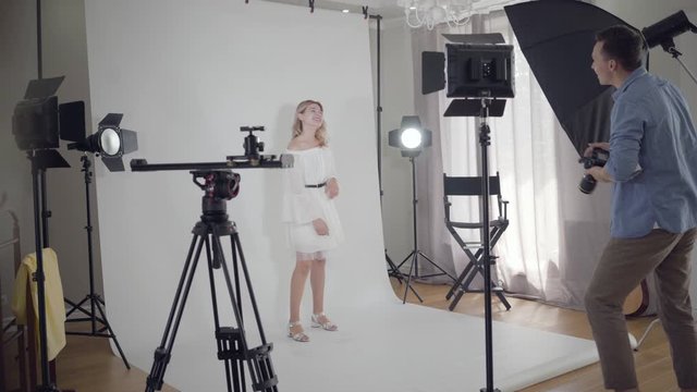 Backstage of the photo shoot. Photographer shakes hands with a model girl standing on white background in the studio before shooting. Fashion magazine studio photoshoot.