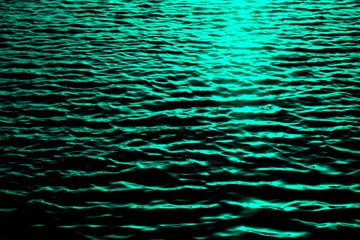 Ripples of sea surface with sun reflections, dark tone image with high contrast and green filter. © Daguimagery