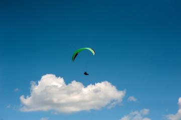 Alone paraglider flying in the blue sky against the background of clouds. Paragliding in the sky on a sunny day.