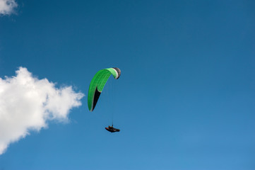 Alone paraglider flying in the blue sky against the background of clouds. Paragliding in the sky on a sunny day.