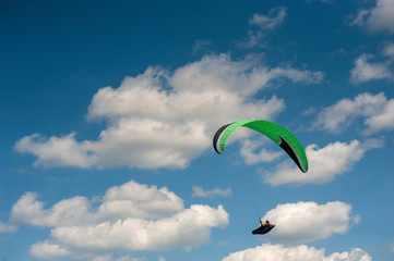 Alone paraglider flying in the blue sky against the background of clouds. Paragliding in the sky on a sunny day.
