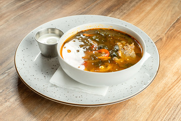 Close up view on restaurant served Green borsch with sour cream, sorrel and meat. Ukrainian cuisine. Tasty soup in white bowl. Food photo for menu or recipe