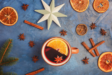 Cup Of Hot Mulled Wine with Spices and Citrus Top View Copy Space Photo. Winter Seasonal Warm Alcohol Beverage in Mug, Slices Orange, Cinnamon Stick and Anise Ingredients Isolated on Blue Background