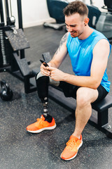 Disabled athlete resting with leg prosthesis. He is texting on his phone