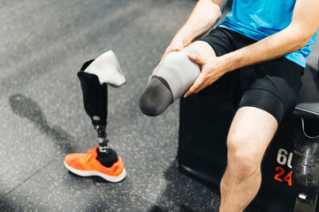 Disabled athlete assembling his leg prosthesis in the gym. Paralympic Sport Concept.