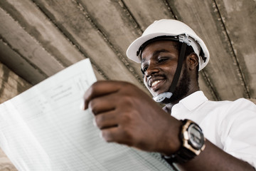 African construction engineer looking at blueprints while wearing helmet