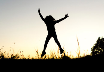 Silhouete of small girl running and jumping on top of the hill