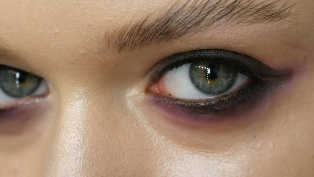 High-fashion. Makeup artist making professional make-up smoky eyes of pink and black color for girl model for shooting in the studio. Close up view of the green eye model