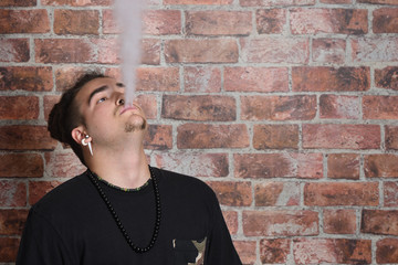 Vaper Smoke outdoor electronic cigarette near the brick wall. Young man smoking big cloud of steam