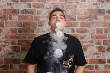Vaper Smoke outdoor electronic cigarette near the brick wall. Young man smoking big cloud of steam