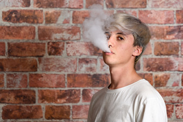 Vaper Smoke outdoor electronic cigarette near the brick wall. Young man smoking big cloud of steam
