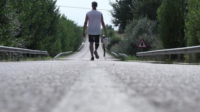 Man walking along the road with a helmet in his hand and a prothesis in his leg