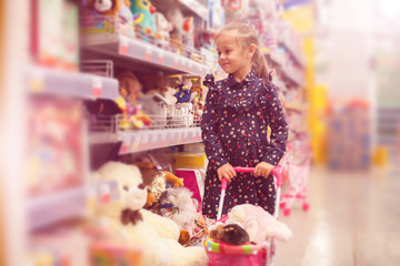 Little girl selecting toys on shelves in supermarket.