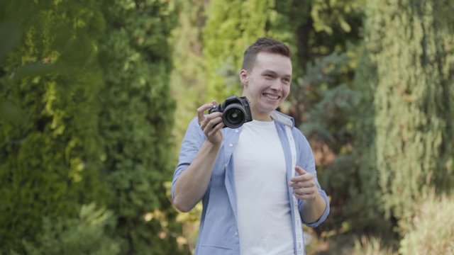 Young professional male photographer in casual clothes taking photo with his camera in the park or garden. Photography, profession, photo session