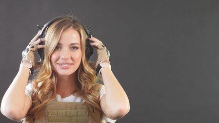 Gorgeous young woman with long blonde hair wearing Military gear, posing isolated in studio over dark background