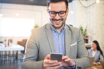 Close-up portrait of smiling businessman using smart phone in office