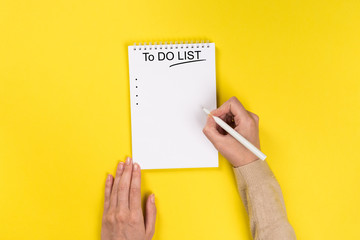 To do list Concept - 2020 number and text on notepad .Woman's hands with perfect manicure holding pencil and  notepad as mockup for your design. Yellow background, flat lay style.