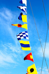 Naklejka premium Marine signal flags set on a sailing mast against of the blue cloudy sky.