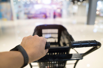 Hand holding cart for shopping at department store interior background.