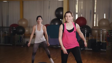 Two female athletes in a sport dress perform a step-up raising of their legs. Stretching and paletes are performed by a professional instructor in a personal lesson.