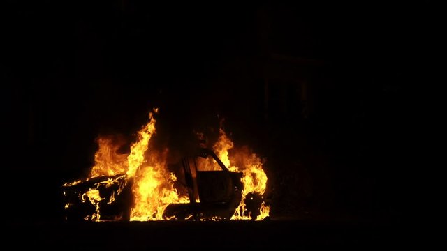 Car on fire burning orange flames, slow-motion shooting. Theme of revenge through damage and destruction of property. Arson of automobile at night.