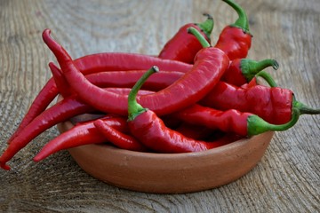 Spicy red peppers in a bowl on a wooden table close-up.