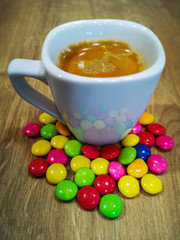 White coffee cup with espresso coffee with colorful chocolates on wooden table