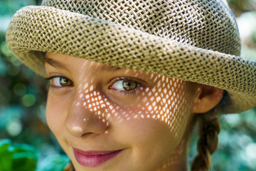 Caucasian child with wicker hat in summer time. Green eyes and light reflection on her cheek.