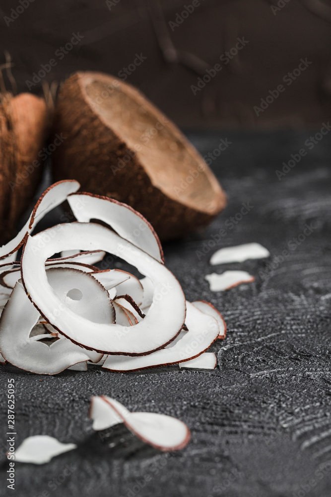 Wall mural coconut chips on a black background, in the background two coconuts