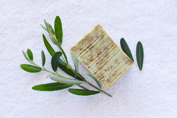 Handmade soap bars and olive branches on a white towel. Top view