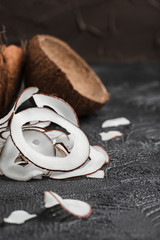 Coconut chips on a black background, in the background two coconuts