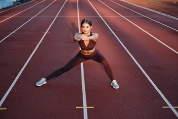 Obraz premium Beautiful sporty girl in sportswear doing stretching exercises on stadium. Fitness woman doing warm up workout outdoor