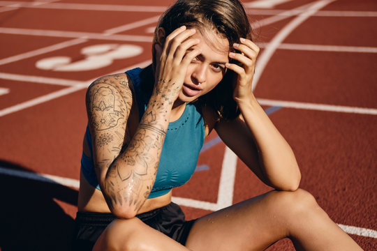Beautiful wet athlete girl in sportswear sensually looking in camera while resting after running on city stadium