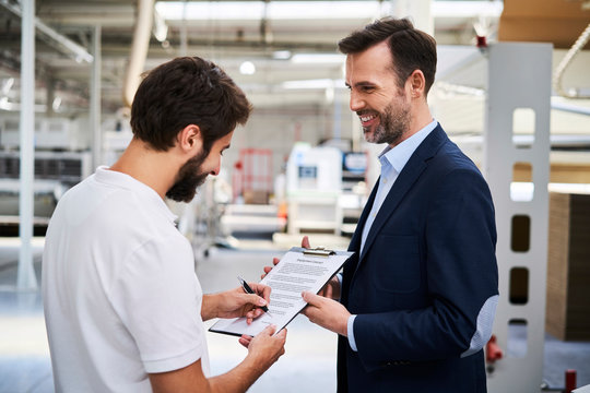 Employee signing document in factory held by businessman
