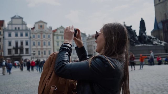 tourist girl in sunglasses takes picture of sights on the phone in the old square of Prague, Czech Republic