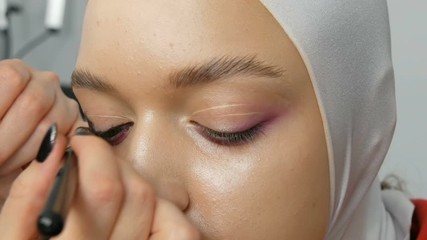 Woman make-up artist stylist makes makeup fashionable pink smoky eyes with special makeup brush of a young model